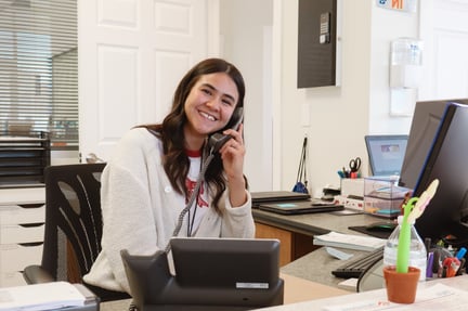 A staff member sitting at the front desk, smiling and holding a phone up to their ear