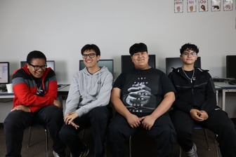A student in a blue graduation cap and gown is smiling and holding a sign that says College Bound