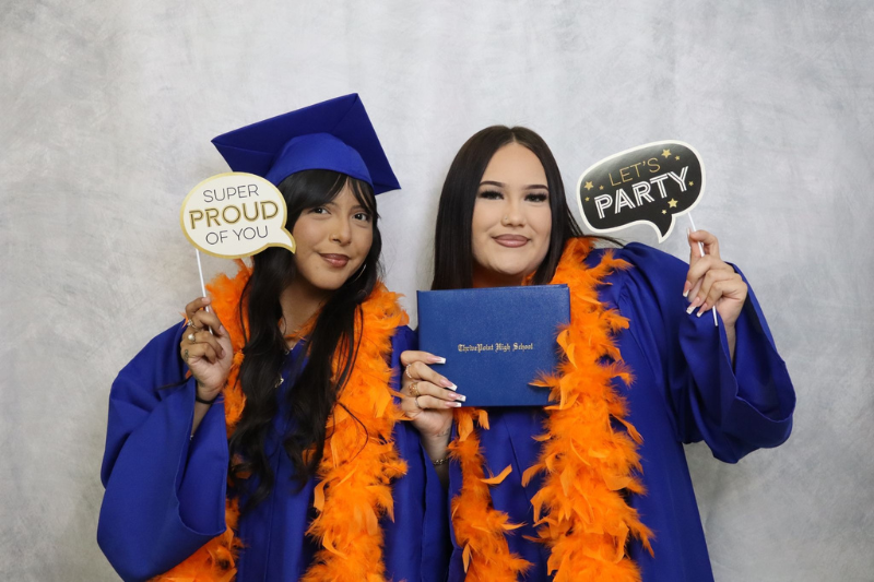 two students wearing blue graduation cap and gowns holding signs